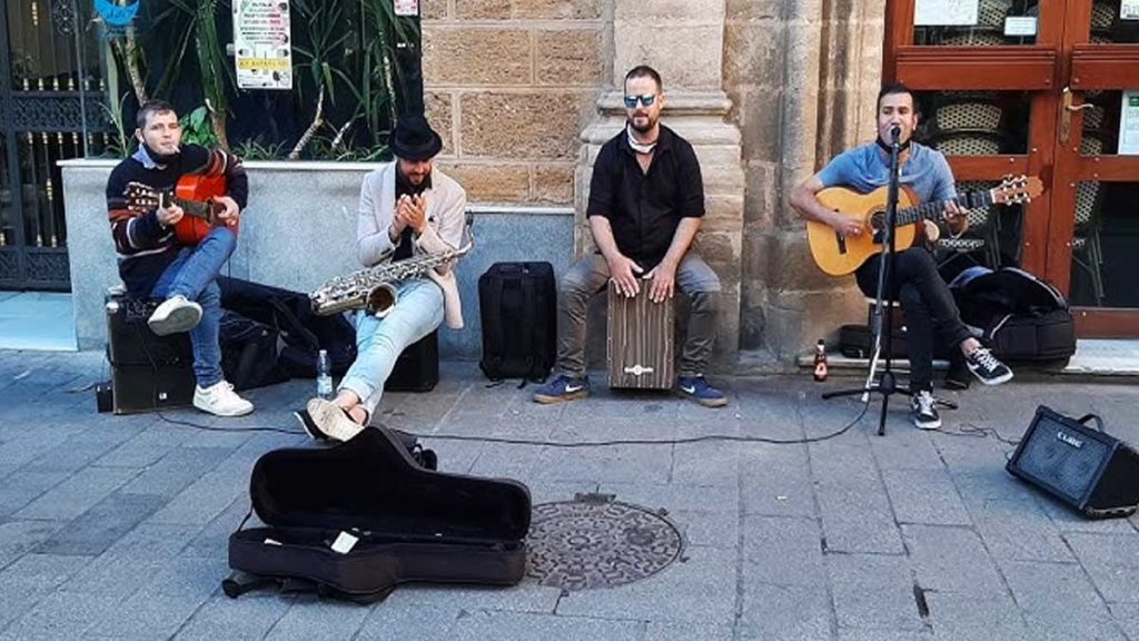 Un grupo de músicos sentados en una calle de Sevilla tocando y cantando.