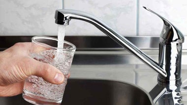 Grifo echando agua y una mano con un vaso bajo él.