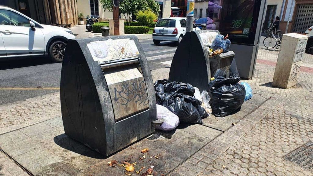 Contenedores llenos y bolsas de basuras en el exterior.