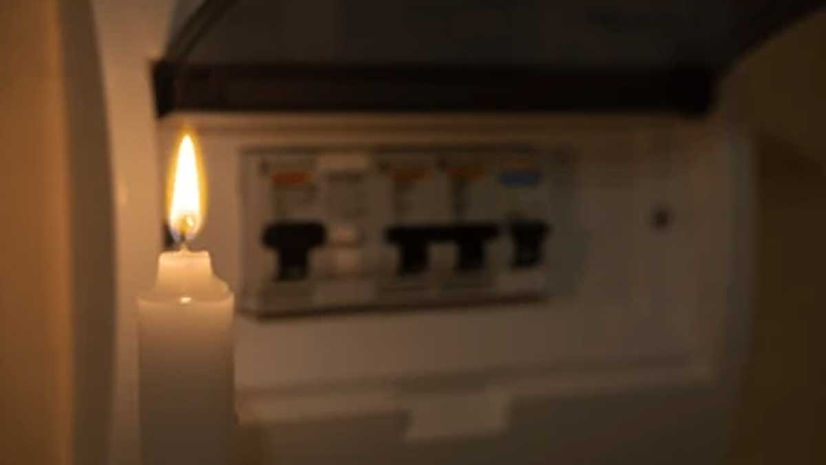 Una vela a la izquierda y un cuadro eléctrico de fondo.