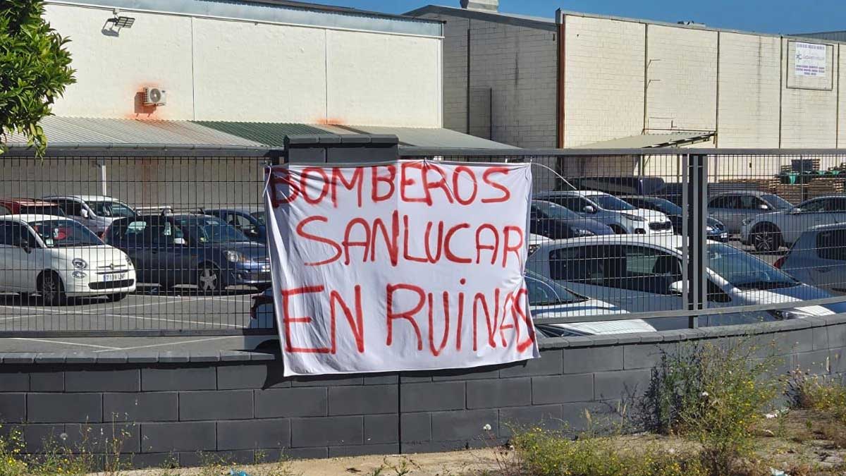 Vaya con una pancarta que dice "Bomberos Sanlúcar en ruinas" con letras rojas.