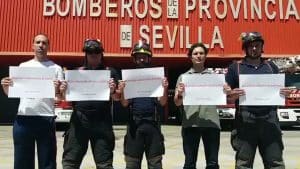 Cinco bomberos posan delante de la puerta del hangar con un papel en las manos cada uno que pone: "Condenados a salvar vidas".