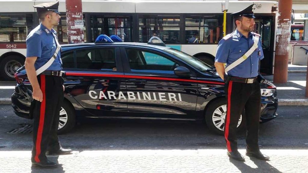 Carabinieri vestidos de uniforme con un coche tras de ellos con el cartel de "carabinieri", Policía.