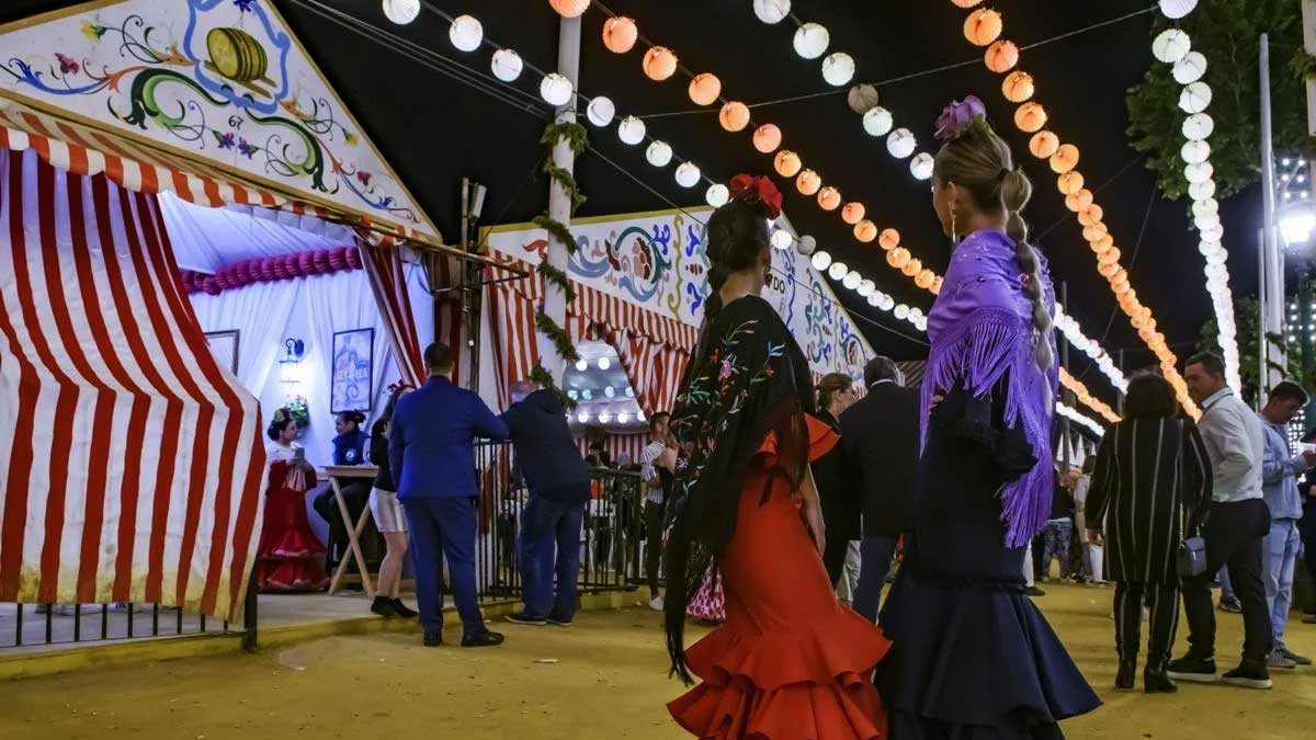 Dos chicas vestidas de gitana frente a unas casetas en la Feria de Sevilla.
