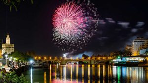 Fuegos rosados de artificio estallando en el cielo de Sevilla, abajo el río Guadalquivir y la Torre del Oro.