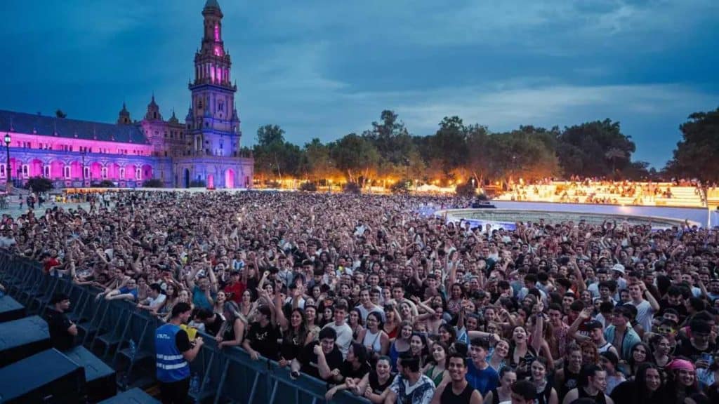 Miles de personas en la Plaza de España dentro del Icónica Sevilla Fest, la Torre Sur iluminada en rosa.