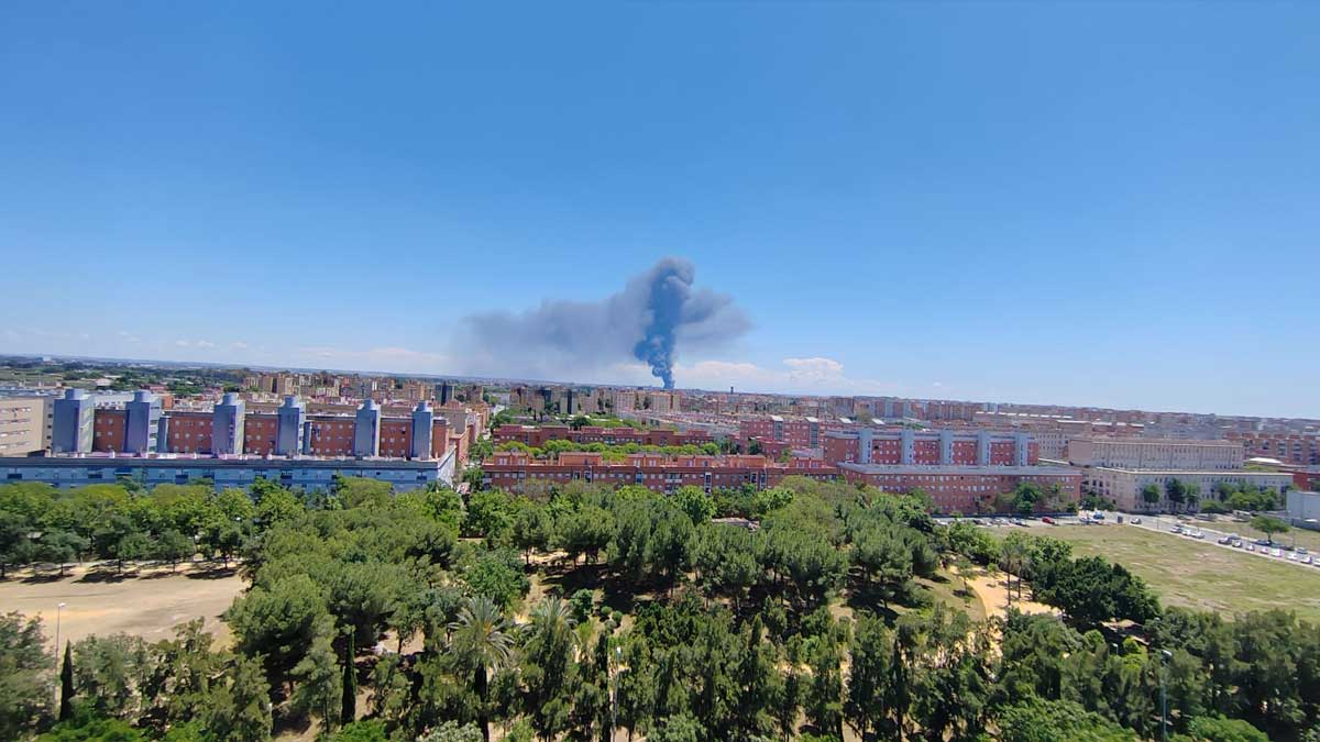Cielo azul de Sevilla destacando la columna de humo gris y los bloques color tierra en la parte baja.
