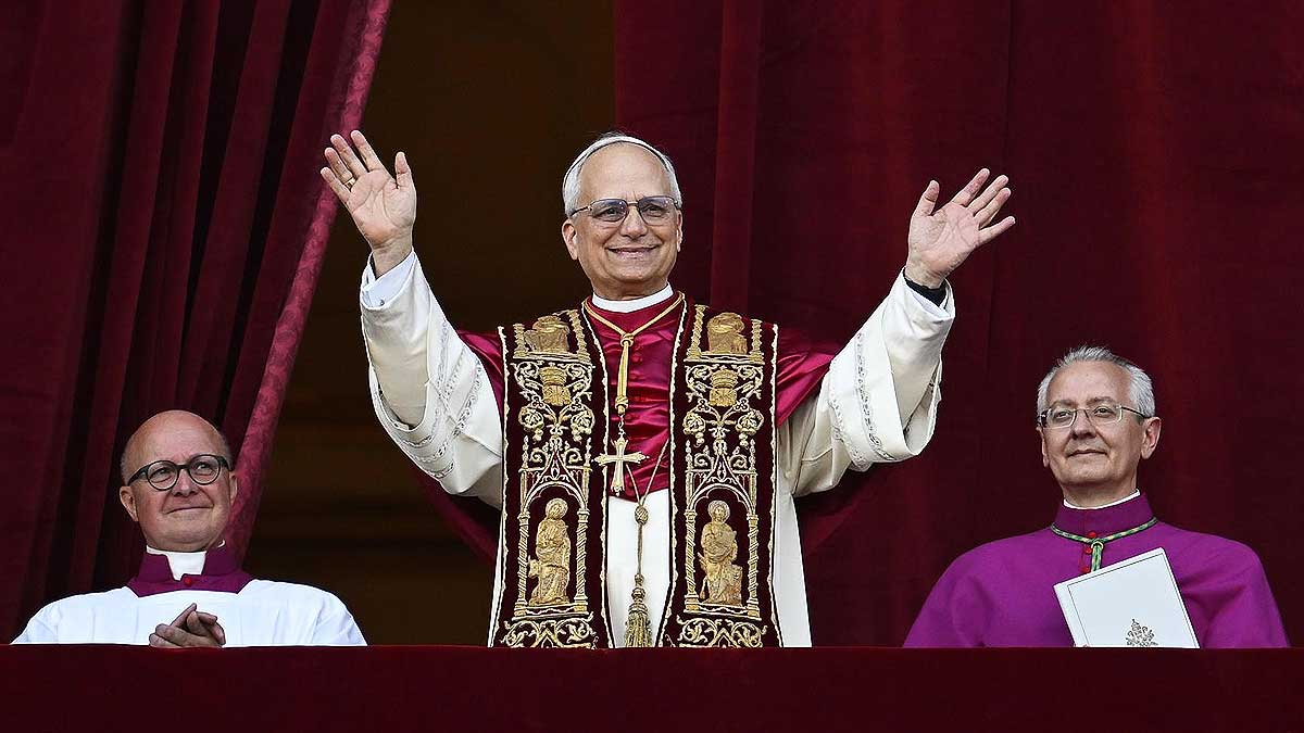 El nuevo Papa León XIV con el traje papal desde el balcón, escoltado por dos cardenales más atrás.