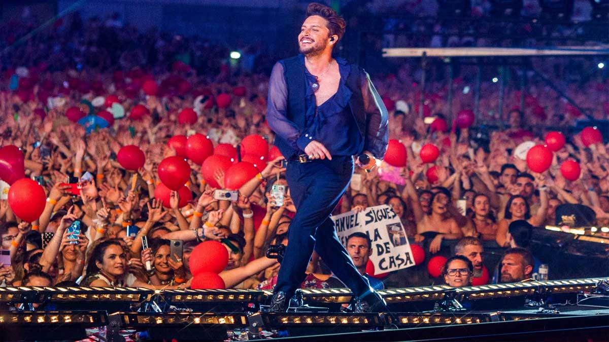 El cantante Manuel Carrasco de negro en una pasarela, los fans con globos rojos en las manos.