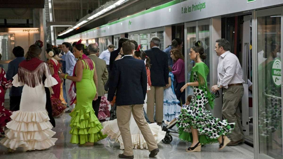 Pasajeros bajándose del metro de Sevilla en una parada, muchas mujeres lucen traje de flamenca.