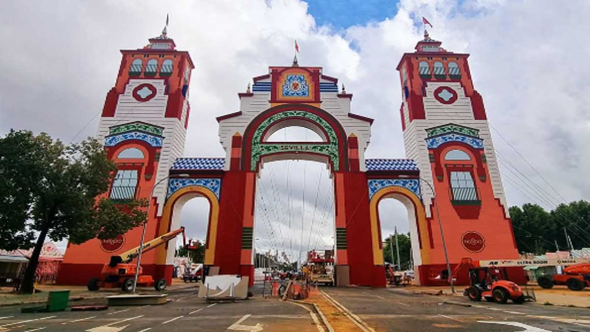 Portada de la Feria de Sevilla con tonos anaranjados y almagra, al fondo el cielo y nubes.