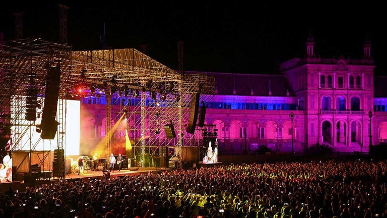 Escenario de Icónica iluminado y de fondo de Plaza de España con focos en tonos rosados.