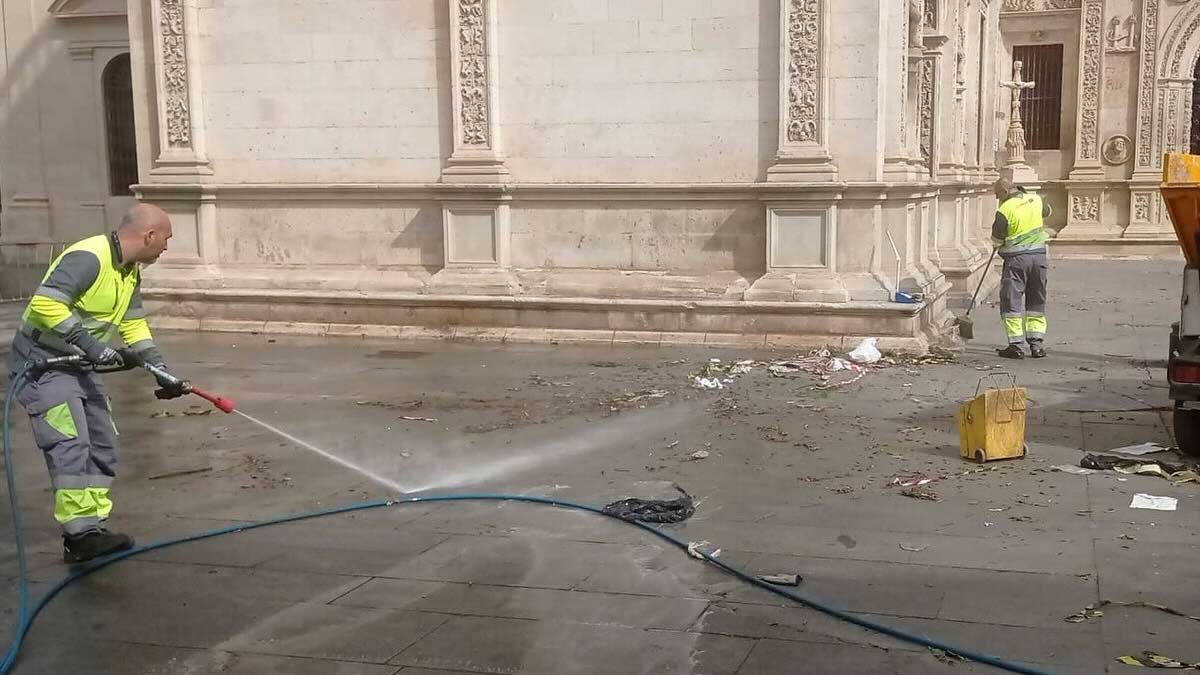 Baldeo de la zona anexa al Ayuntamiento de Sevilla por dos operarios con mangueras a presión.