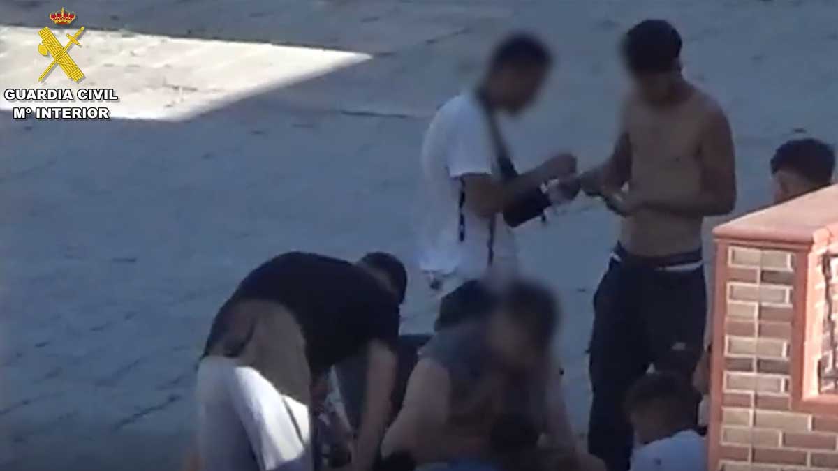 Varios jóvenes en la calle, dos trapichean con drogas.