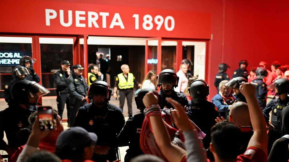 Muchos aficionados protestando ante una puerta, en rojo, con el rótulo 1890.