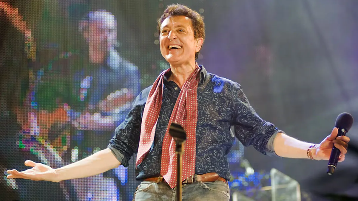 Manolo García con camisa azul y pañuelo color caldera en el cuello cantando.