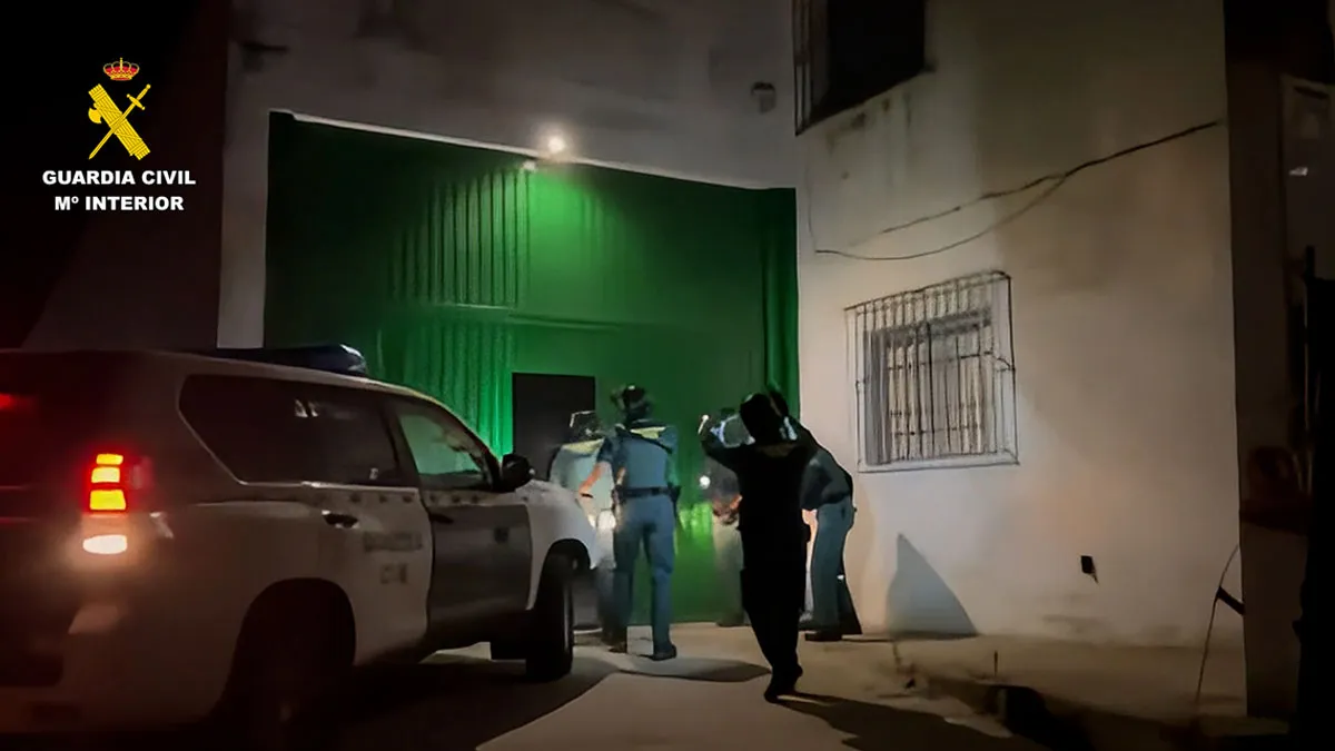 Varios agentes de la Guardia Civil entran en una nave con el portón verde.