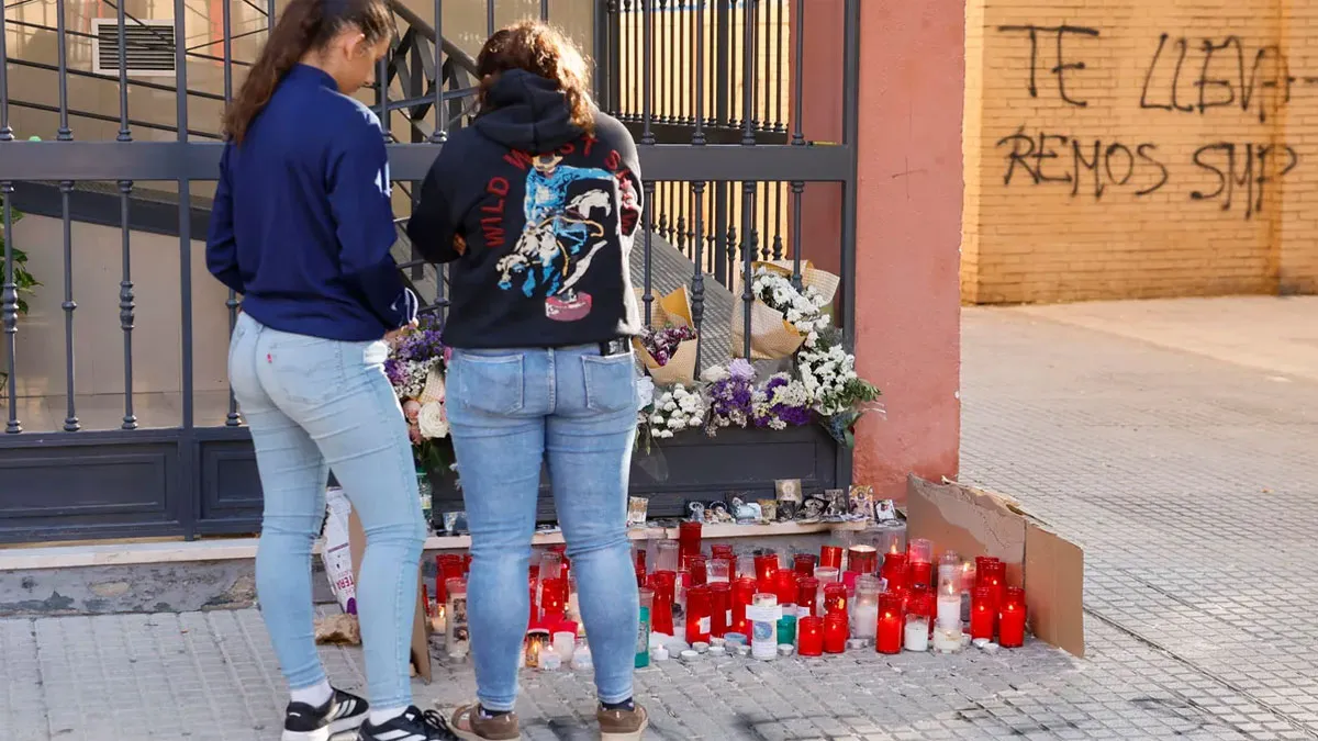 Dos chicas ponen unas velas ante el portal de Sandra Peña y tras ellas el muro pintado del colegio.