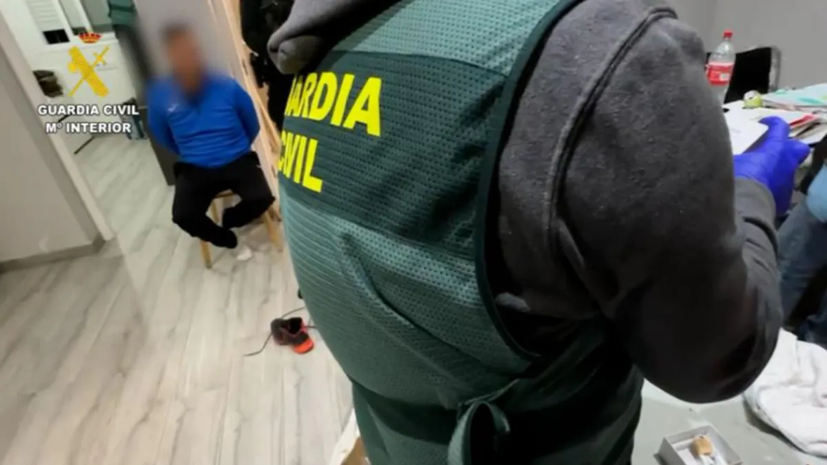Agente de la Guardia Civil y detenido al fondo esposado a una silla.