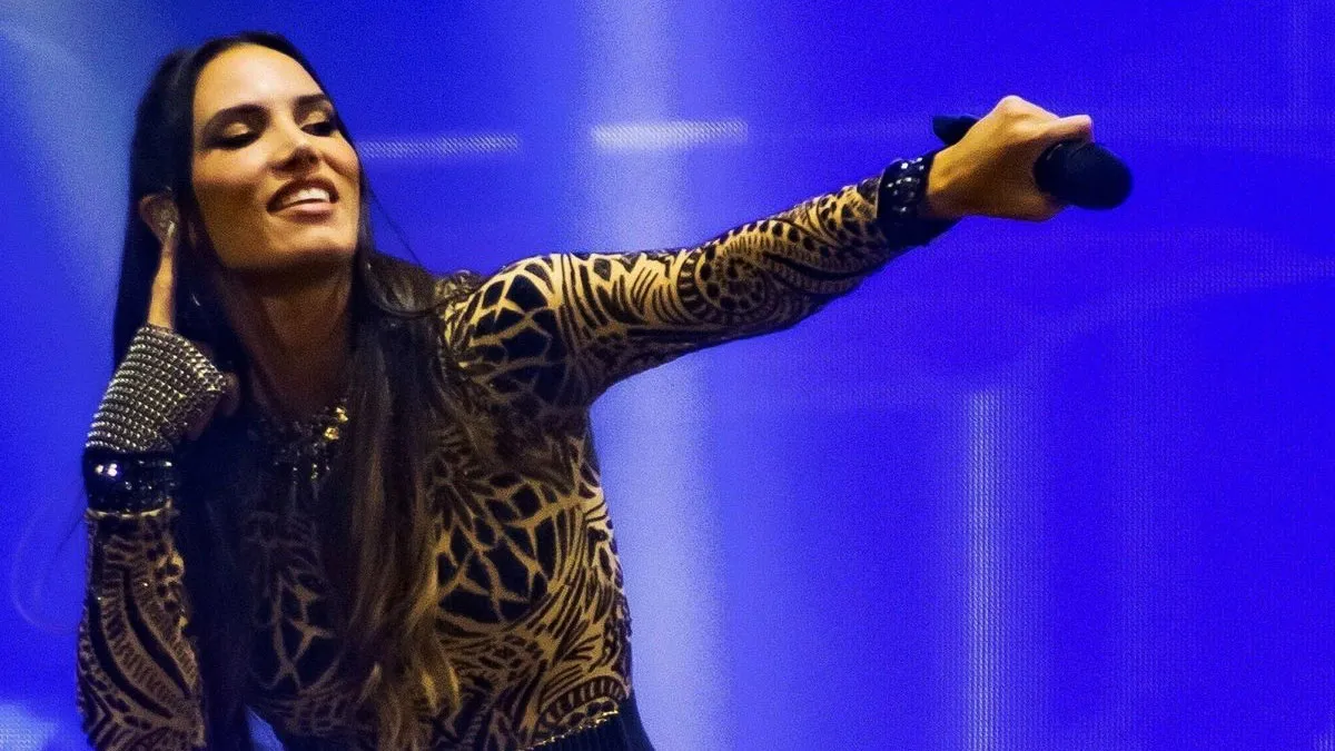 India Martínez cantando en un escenario con fondo azul.