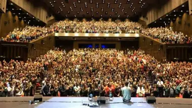 Gradas llenas de público en Cartuja Center, en el escenario una persona sentada.