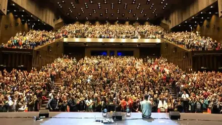 Gradas llenas de público en Cartuja Center, en el escenario una persona sentada.