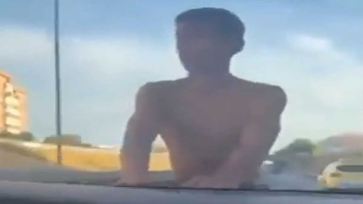 Joven sin camiseta en el capó de un coche en la SE-30 de Sevilla.