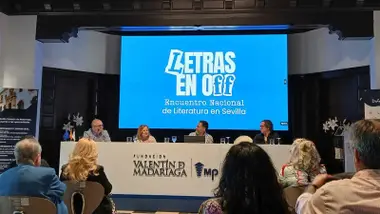 Mesa con personas sentadas y un cartel en azul y blanco que pone "Letras en Off".
