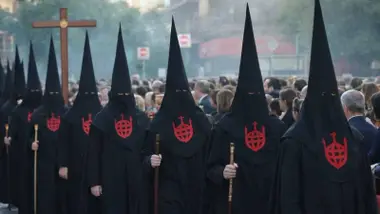 Fila de nazarenos del Santo Entierro con túnica negra y escudo rojo.