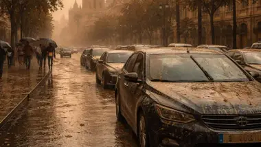 Coches en una avenida cubiertos de arena y barro.