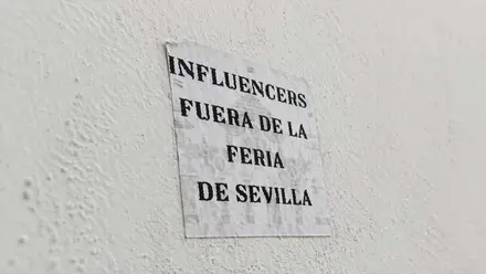 Cartel pegado en una pared donde se puede leer: "Influencers fuera de la Feria de Sevilla".