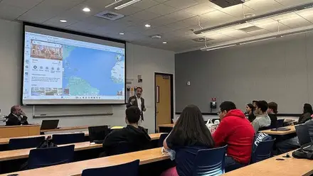 Clase en la que una persona explica, sobre mapa, la importancia de la conexión Sevilla y Miami.