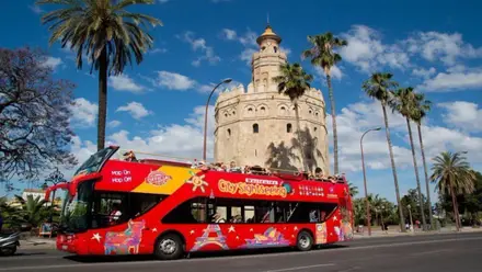Autobús turístico en rojo pasando por la Torre del Oro.
