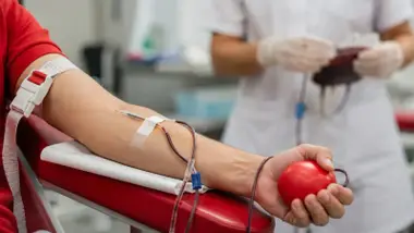 Persona donando sangre, sostiene en la mano una pelota roja.