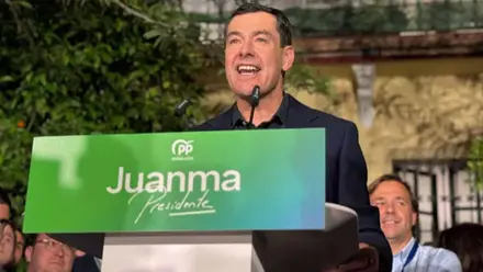Juanma Moreno, en un atril con su nombre en verde y blanco, hablando a los seguidores.