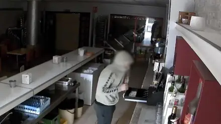 Ladrón con sudadera gris y capucha en pleno robo.
