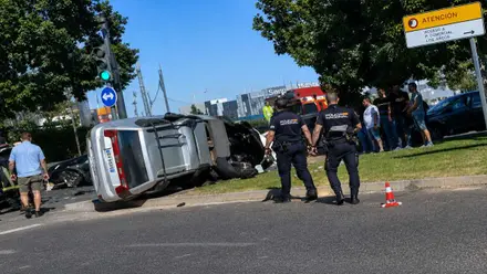 Coche volcado en color plateado con agentes de la Policía Nacional cerca del mismo.