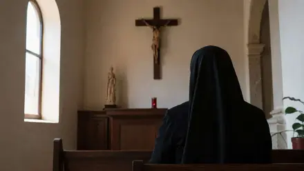 Monja ante un crucifijo. Está de espalda.