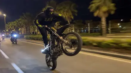 Motorista haciendo el caballito con su moto por una vía urbana.