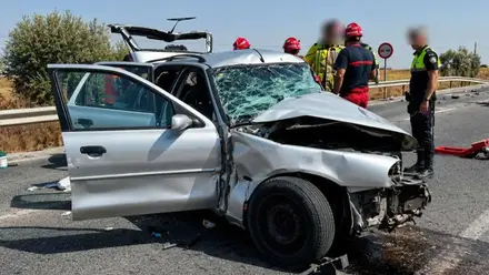 Automóvil de color plateador totalmente destrozado tras el accidente, a su lado efectivos de bomberos.