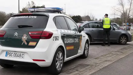 Un coche de la Guardia Civil en primer plano y u agente solicitando la documentación a un conductor.
