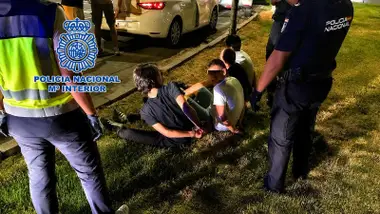 Agentes de la Policía Nacional detienen a unos ladrones que están esposados en el césped.