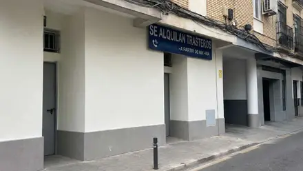 Calle con los trasteros y el acceso, hay un cartel azul con letras blancas sobre la puerta.