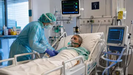 Enfermera cuida a un paciente en la cama de un hospital, en una UCI.