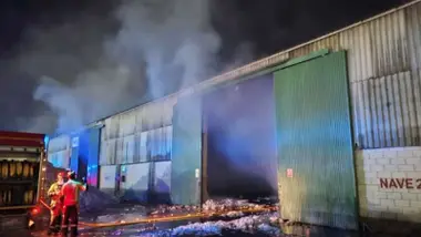 Bomberos y la nave incendiada con algodón en su interior.